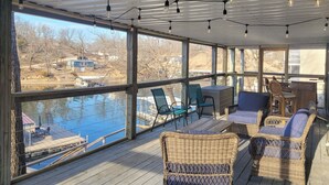 A covered outdoor deck with wicker furniture, a table, and chairs, overlooking a body of water and a dock. - Waterfront Home w/ 3 Decks on Lake of the Ozarks! (Sunrise Beach)