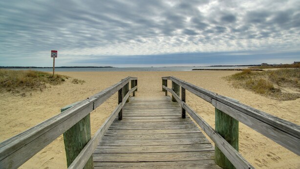 A wooden boardwalk leading to a sandy beach with a cloudy sky. - Cape Cod Family Home w/ Yard: Walk To Beach! (West Yarmouth)