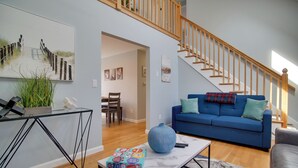 A modern living room with a blue sofa, a coffee table, and a staircase. - Cape Cod Family Home w/ Yard: Walk To Beach! (West Yarmouth)