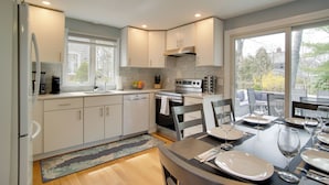 A modern kitchen with white cabinets, a built-in oven, and a dining area with a table set for four. - Cape Cod Family Home w/ Yard: Walk To Beach! (West Yarmouth)