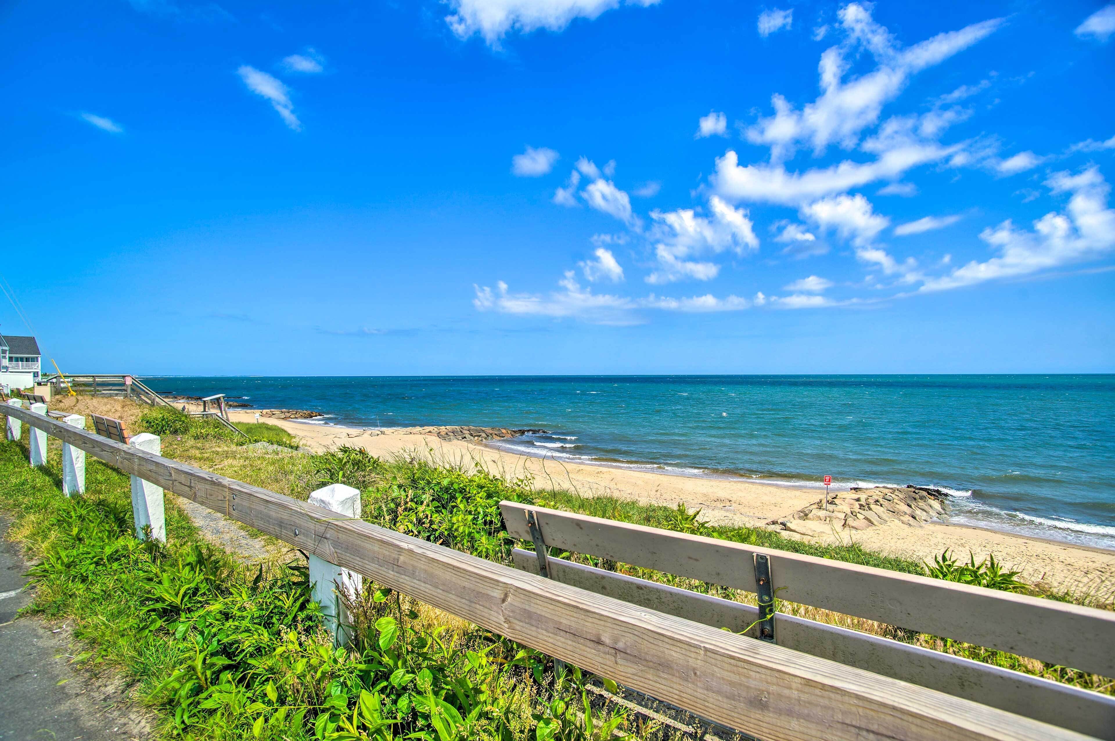 A beach with a wooden walkway and a bench, leading to the ocean.