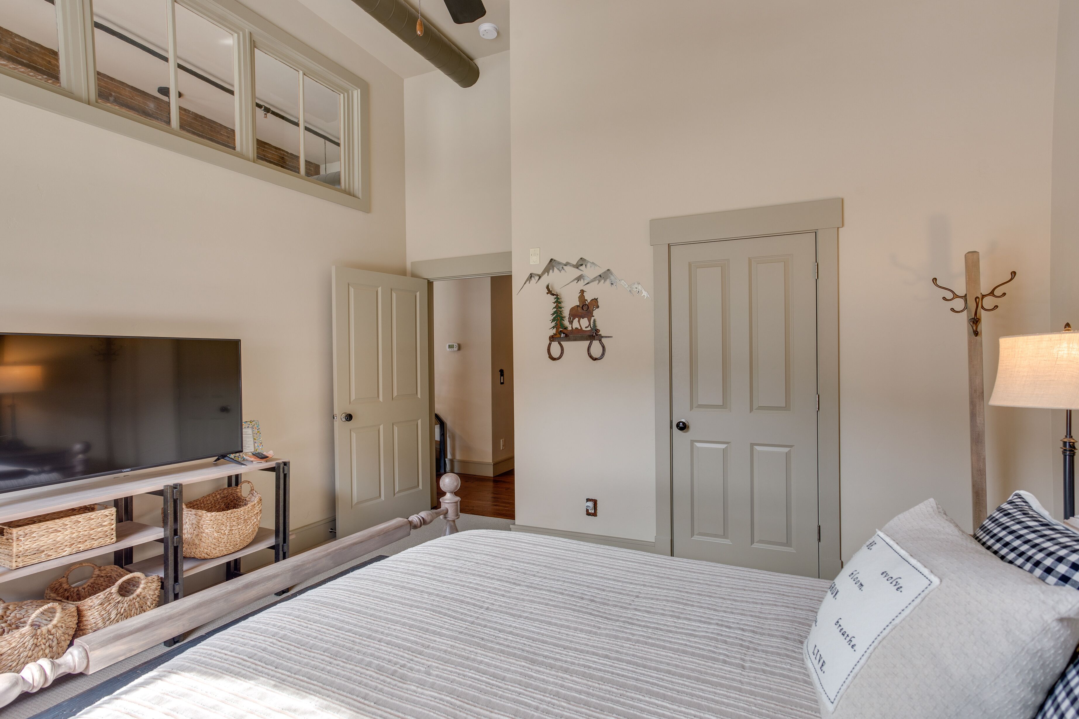 A bedroom with a bed, a TV on a stand, a door, and a wall decoration.