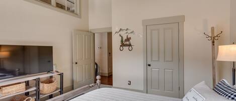 A bedroom with a bed, a TV on a stand, a door, and a wall decoration.