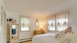 A bedroom with a bed, a dresser, a mirror, and a window with curtains. - Charming West Yarmouth Home ~ 2 Mi to Beach! (West Yarmouth)