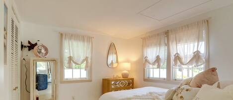A bedroom with a bed, a dresser, a mirror, and a window with curtains.