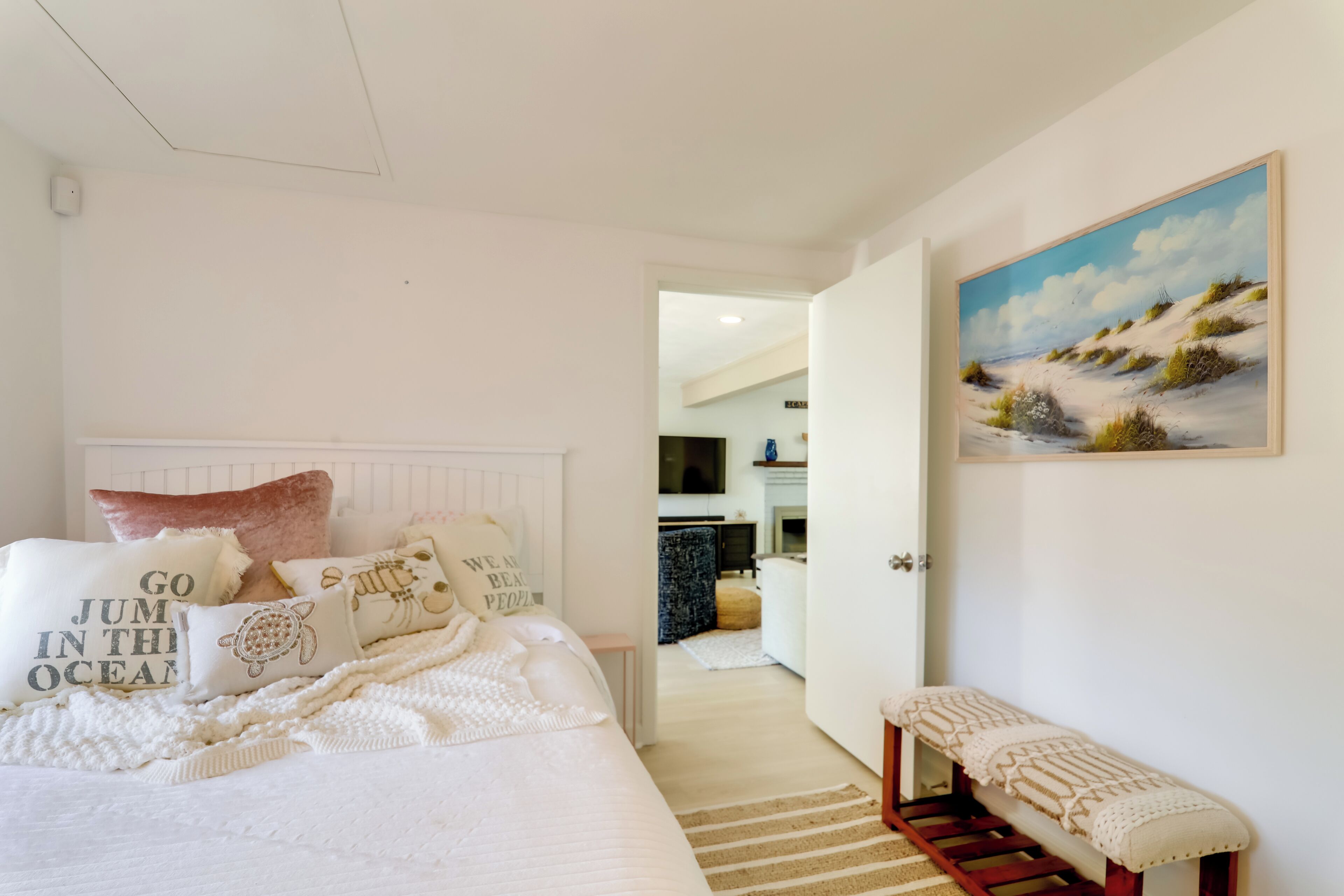 A bedroom with a bed, pillows, a bench, and a painting on the wall.