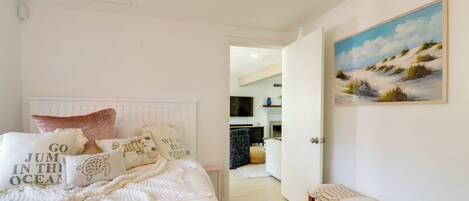 A bedroom with a bed, pillows, a bench, and a painting on the wall.