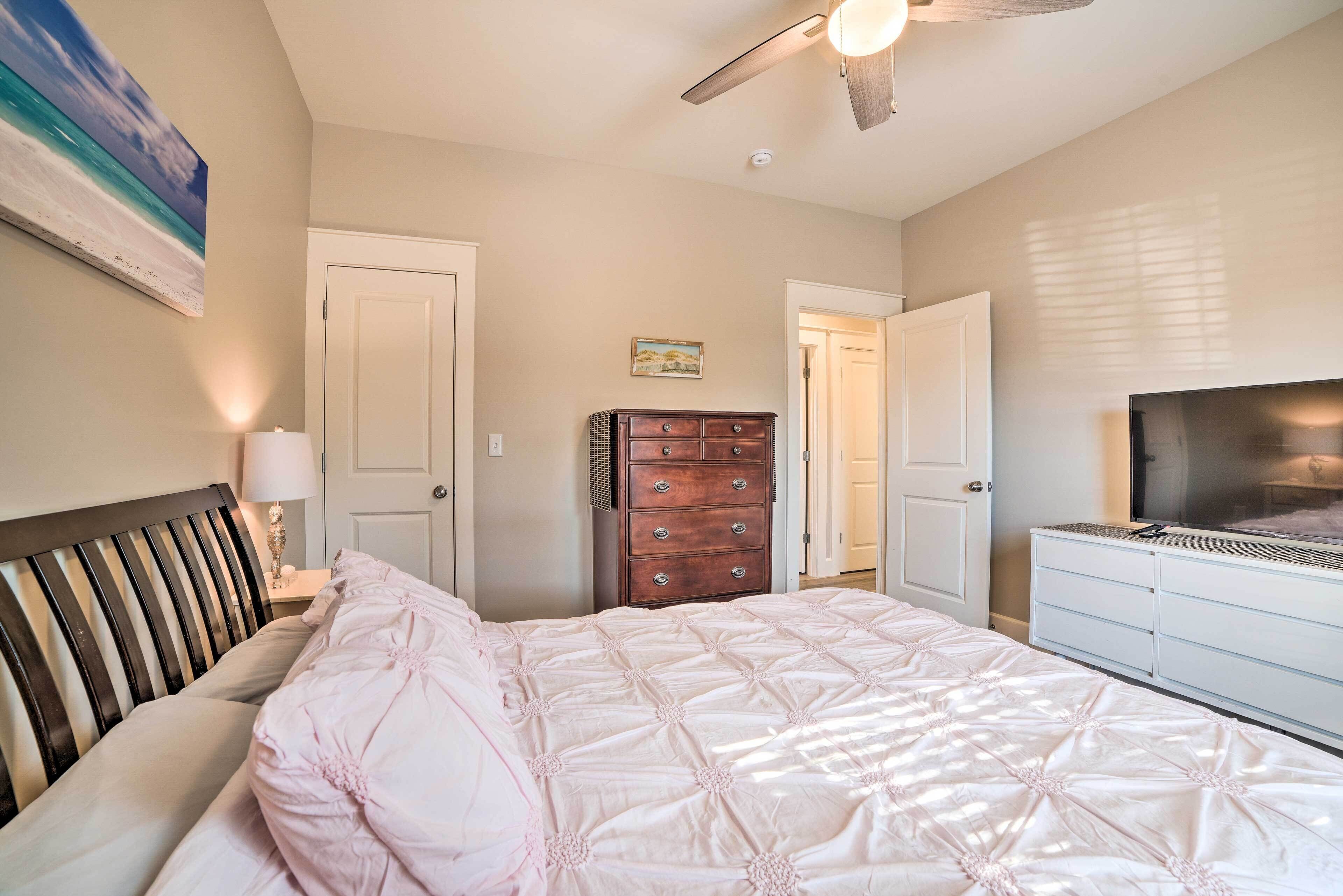 A bedroom with a bed, dresser, TV, and ceiling fan.