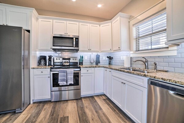 A modern kitchen with white cabinets, stainless steel appliances, a granite countertop, and a window with blinds.