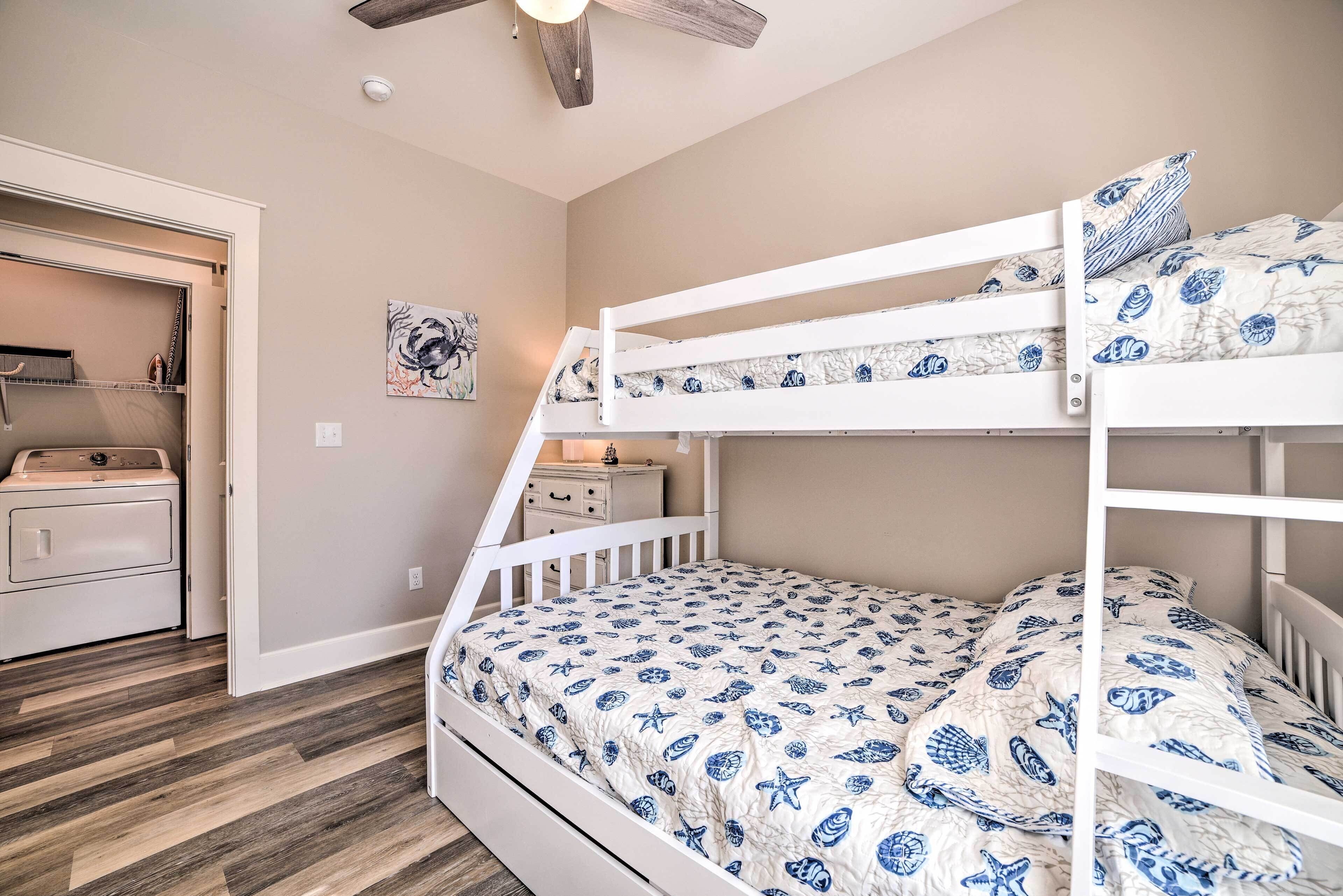 A bunk bed with a patterned bedspread, a ceiling fan, and a small dresser with a mirror.