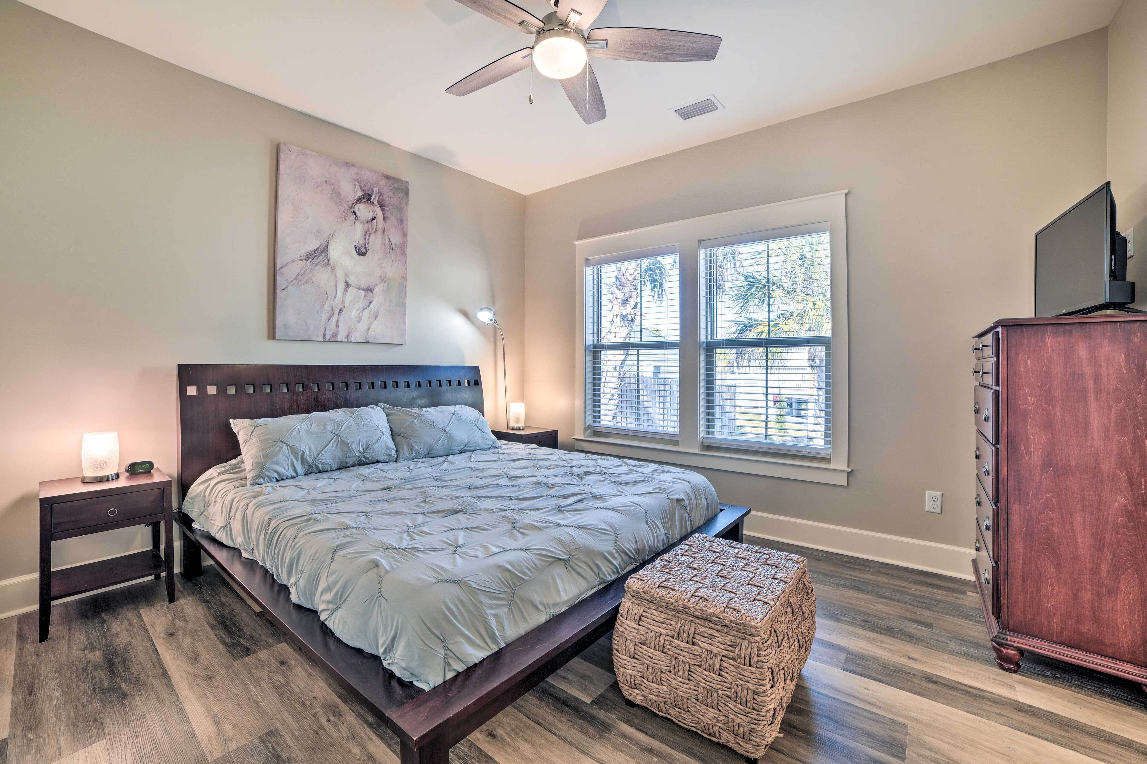 A bedroom with a bed, a nightstand, a lamp, a wooden dresser, and a window with blinds.