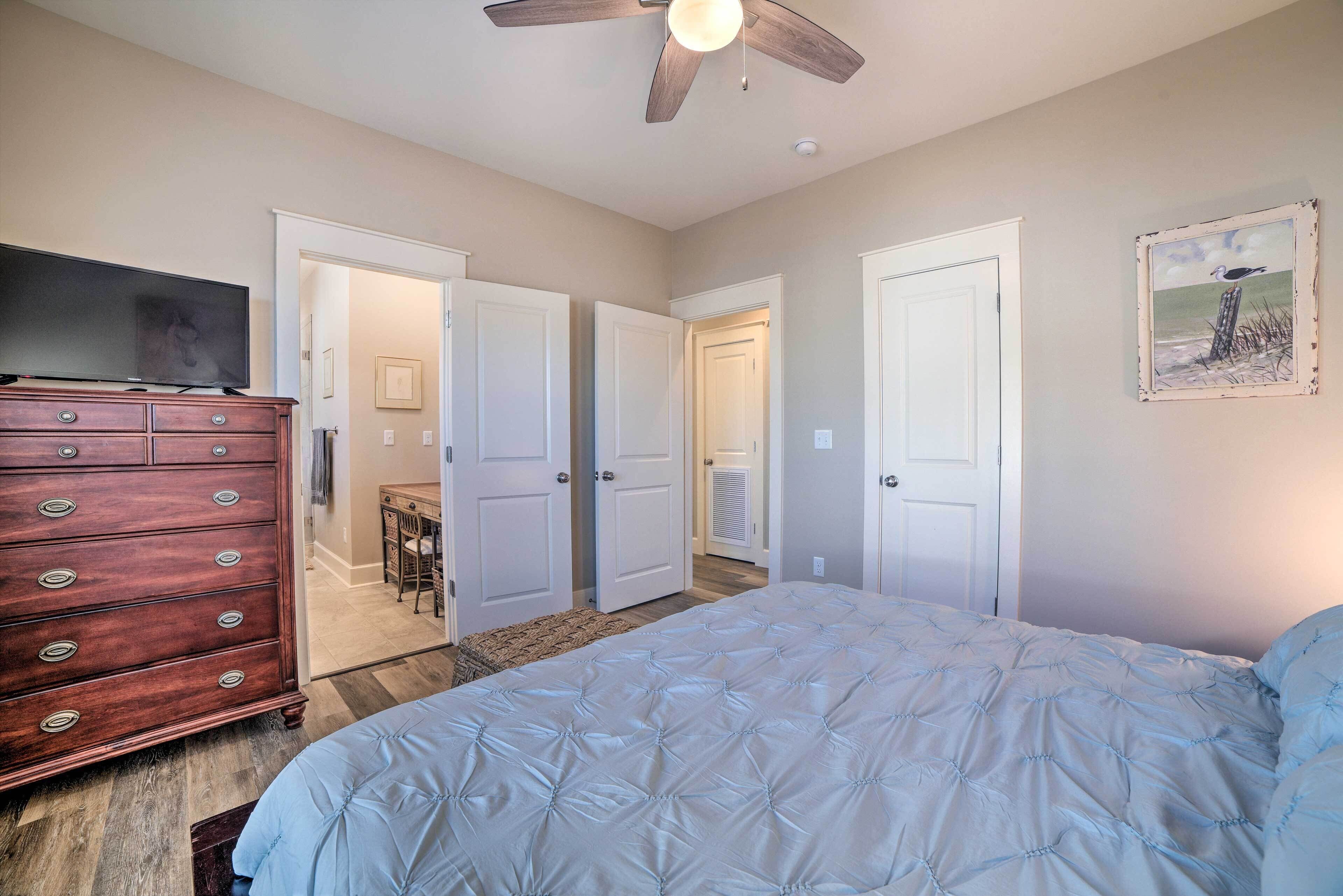 A bedroom with a bed, dresser, television, and ceiling fan.
