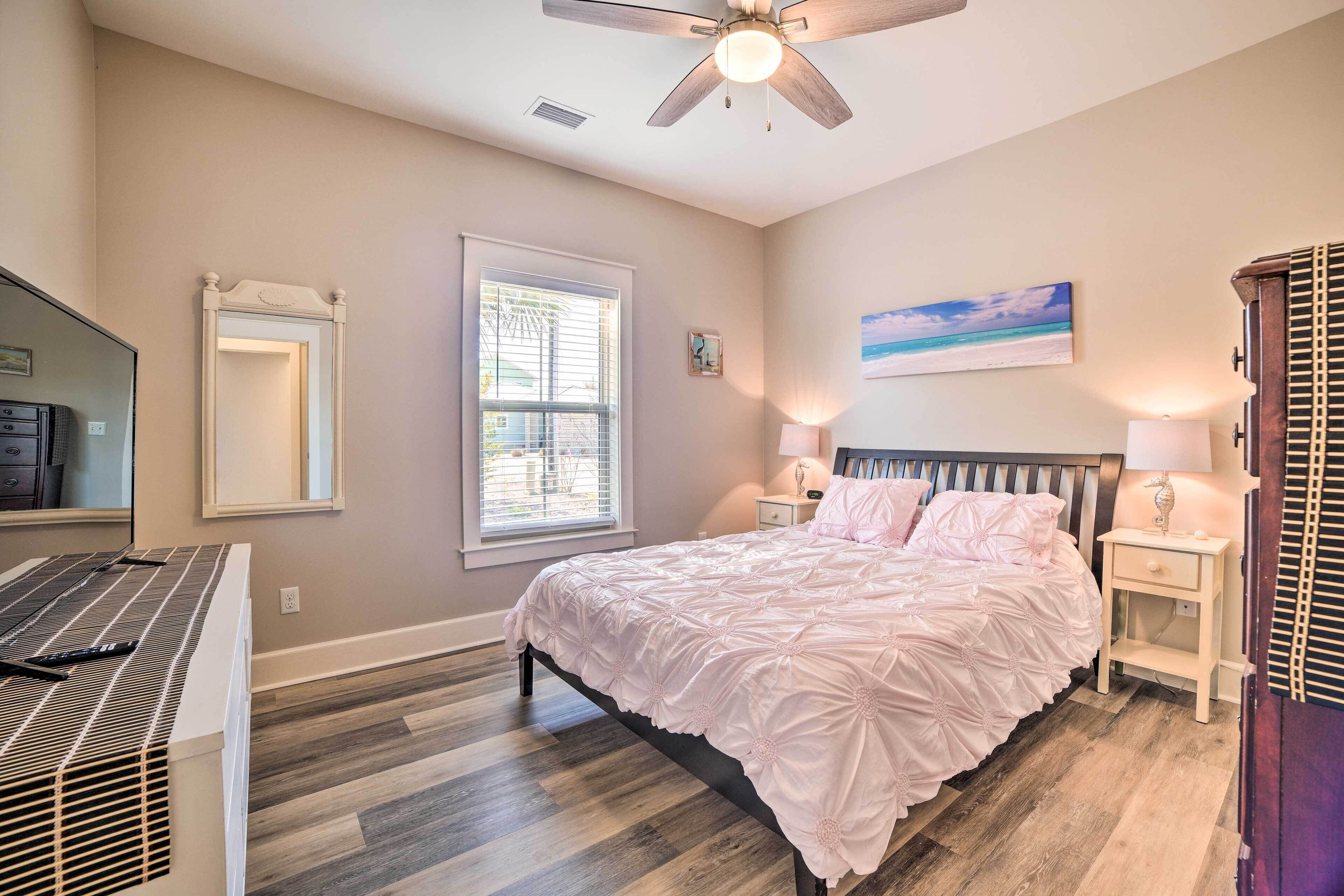 A bedroom with a bed, bedside lamps, a ceiling fan, a window, and a painting on the wall.