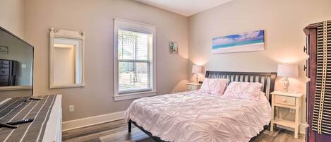 A bedroom with a bed, bedside lamps, a ceiling fan, a window, and a painting on the wall.