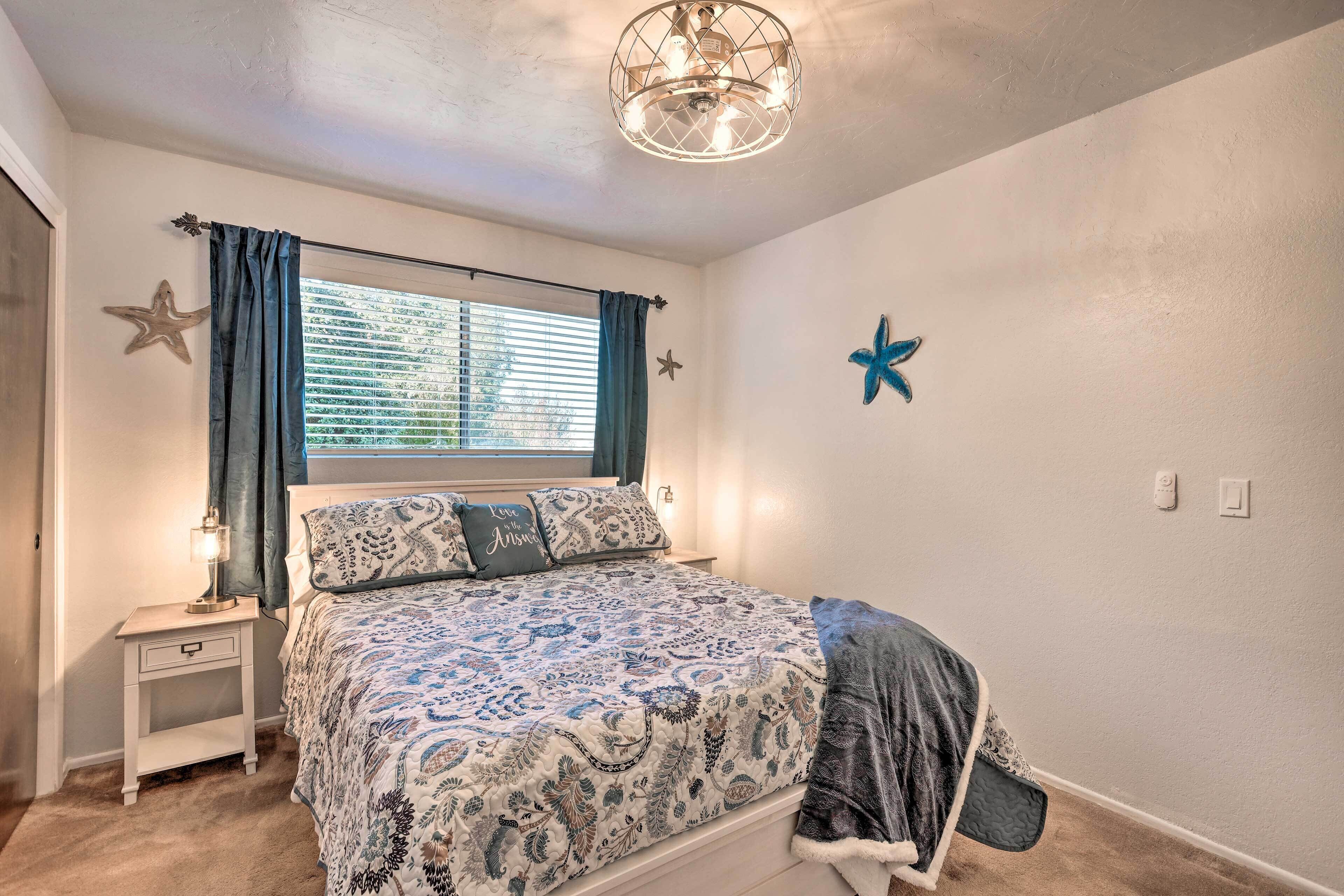 A bedroom with a bed, a nightstand, a window with curtains, a starfish decoration, and a ceiling light fixture.
