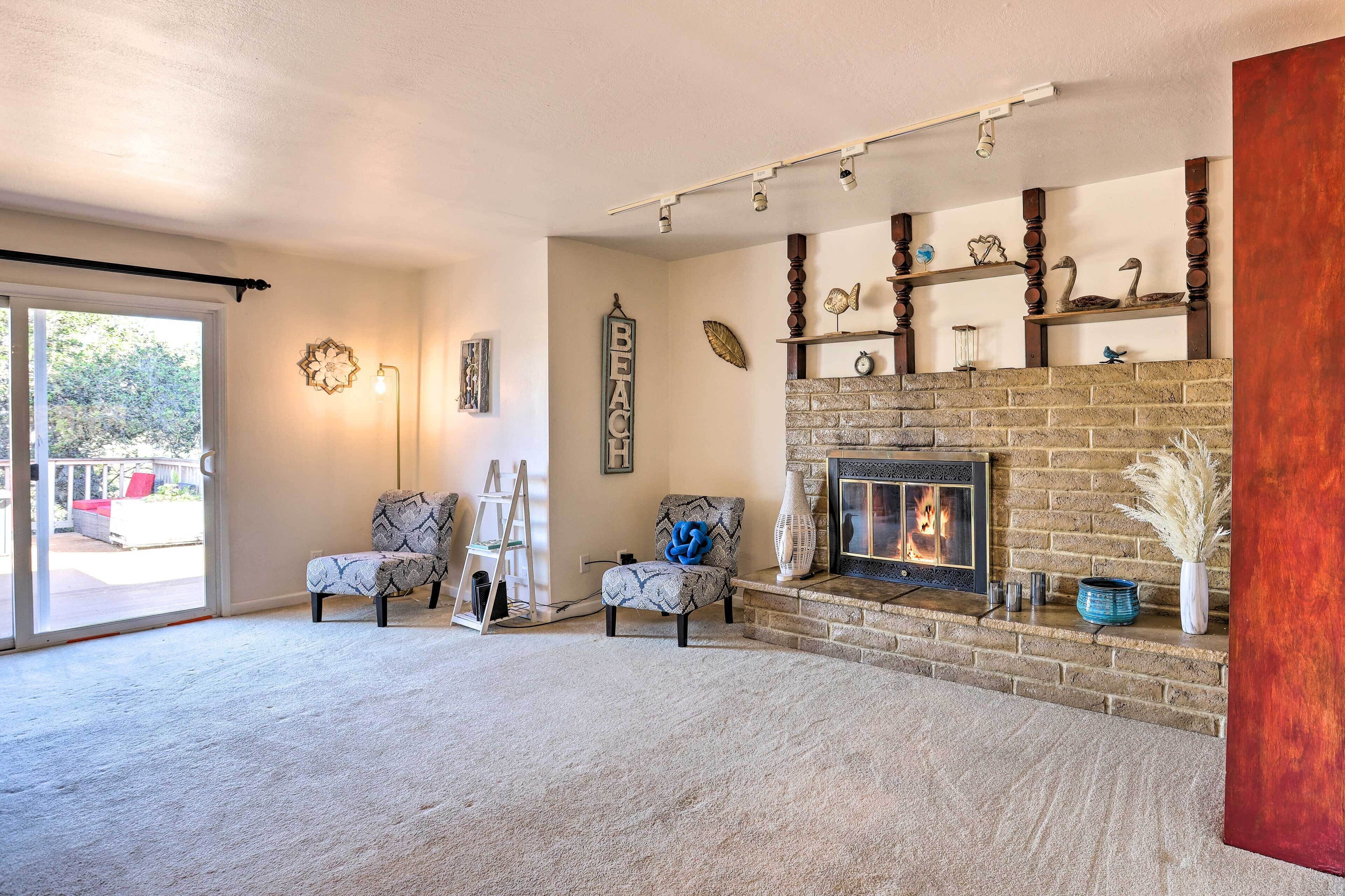 A living room with a fireplace, two patterned armchairs, a ladder, and a large window.