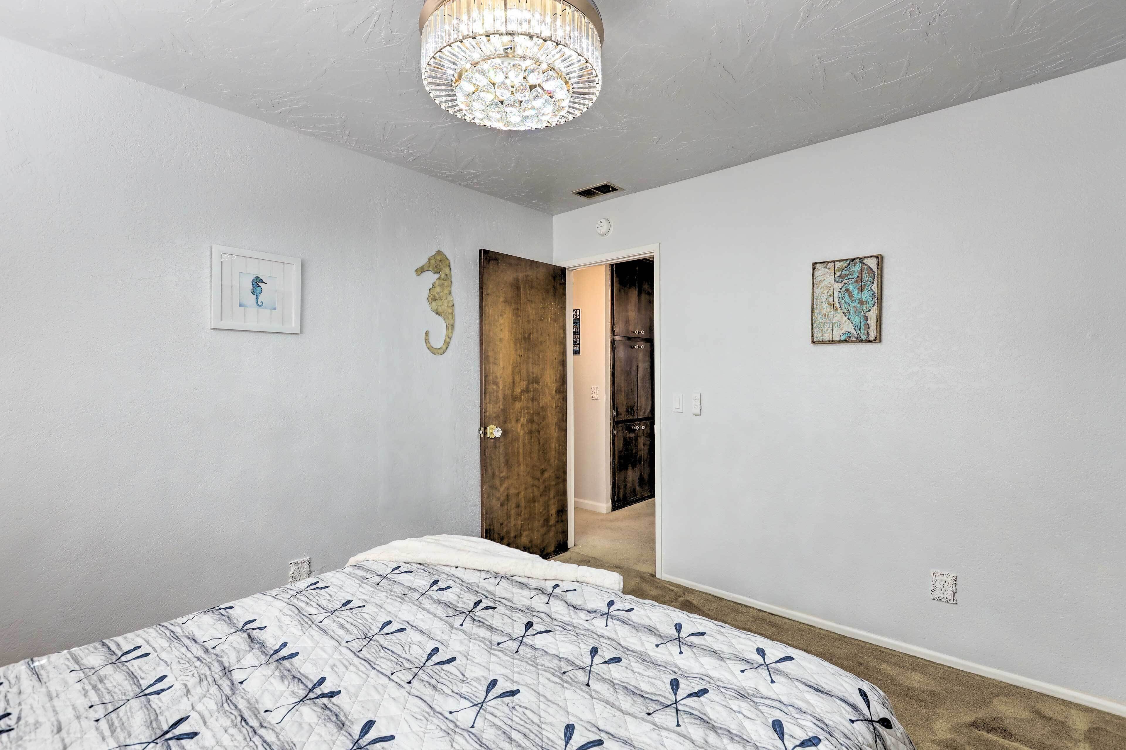 A bedroom with a bed, a chandelier, and a door leading to another room.