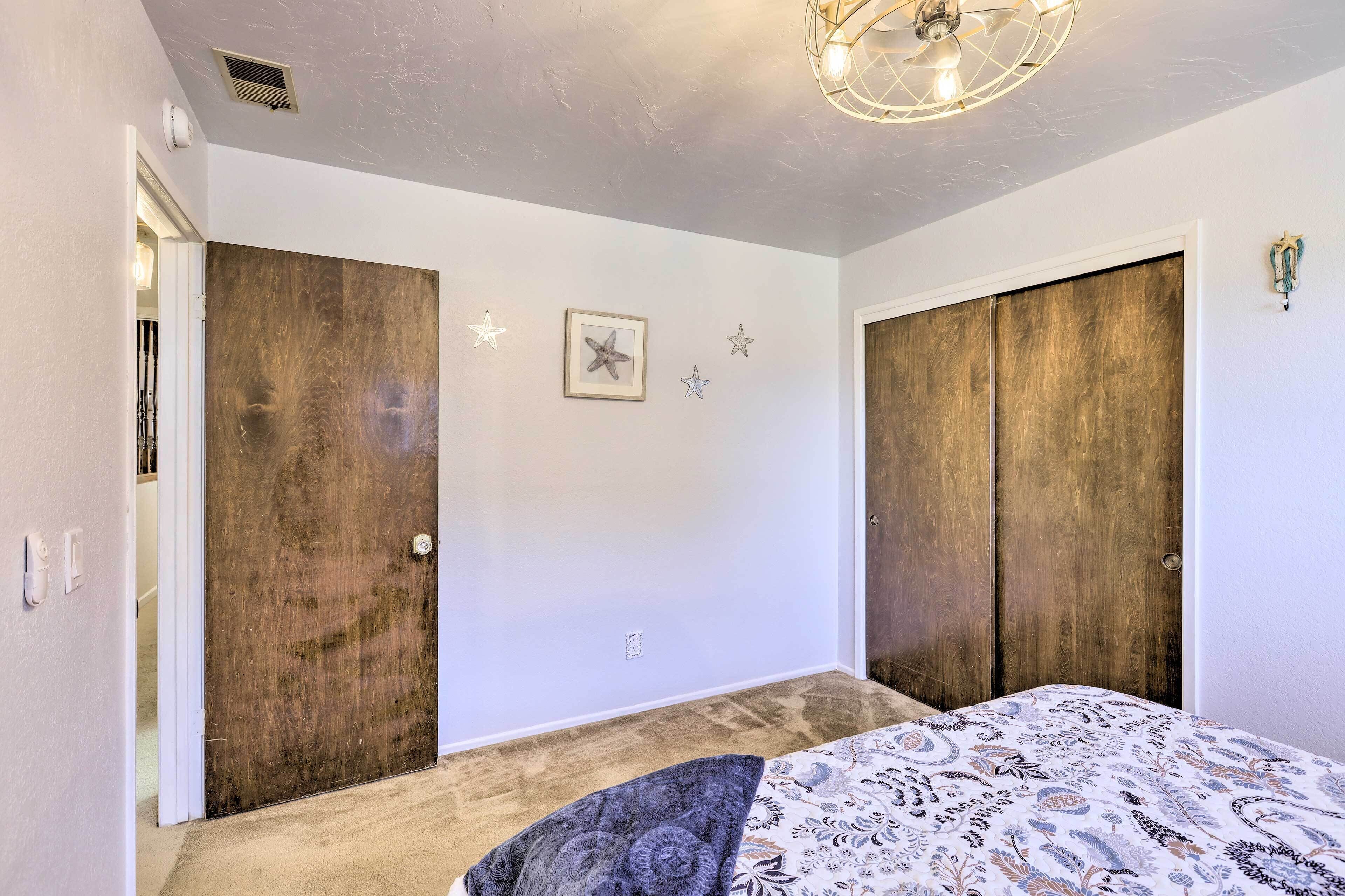 A bedroom with a bed, two wooden wardrobes, a ceiling fan, and a wall-mounted light fixture.