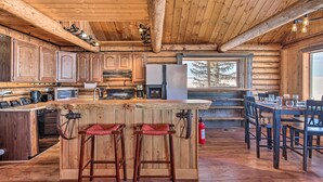 A rustic cabin-style kitchen with wooden cabinets, a large island with stools, and a dining area with a table and chairs.