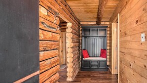 A log cabin interior with a wooden bench, a small seating area with cushions, and a door leading to another room.