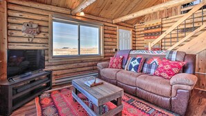 A log cabin interior with a leather couch, wooden coffee table, and a television.