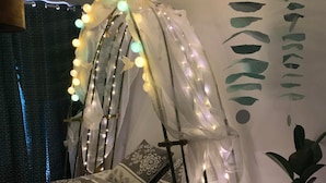 Una cama con dosel, luces decorativas, ropa de cama estampada y una planta en maceta.