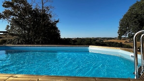 Piscina azul cristalina con cubierta de madera, rodeada de árboles y un cielo despejado.