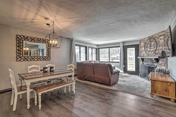 A dining area with a wooden table and chairs, a brown sofa, and a stone fireplace.