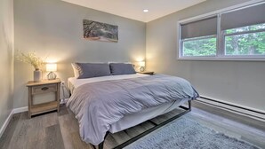 Quarto com cama, mesas de cabeceira, um quadro e janela com vista para árvores.