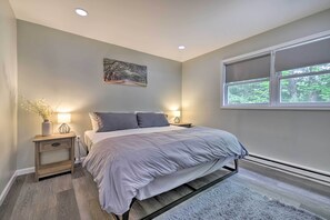 A bedroom with a bed, nightstands, a painting, and a window with a view of trees. - Modern Poconos Home Close to Lake & Amenities (Tobyhanna)
