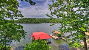 A lakeside cabin with a red roof, dock, and dockside seating area.