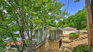 A cabin with a wooden deck and a small porch, surrounded by trees and a body of water.