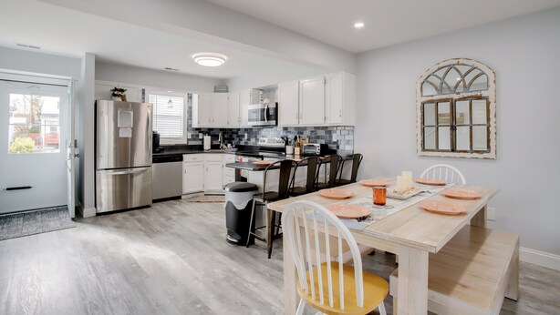 Una cocina moderna con electrodomésticos de acero inoxidable, armarios blancos y una mesa de comedor de madera para cuatro personas.