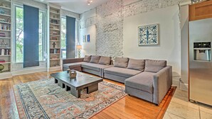 A modern living room with a sectional sofa, a coffee table, and a patterned rug. There are bookshelves, a fireplace, and a brick wall. - Walk to Dtwn Distilleries: Nulu Art District Loft (Louisville)