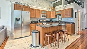A modern kitchen with wooden cabinets, stainless steel appliances, and a central island with bar stools. - Walk to Dtwn Distilleries: Nulu Art District Loft (Louisville)