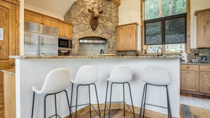 Eine Küche mit Kamin aus Stein, Holzschränken, einem Edelstahlkühlschrank und einer Bar mit Hockern.