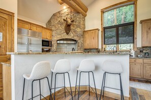 Une cuisine dotée d’une cheminée en pierre, de meubles en bois, d’un réfrigérateur en acier inoxydable et d’un coin bar avec des tabourets.