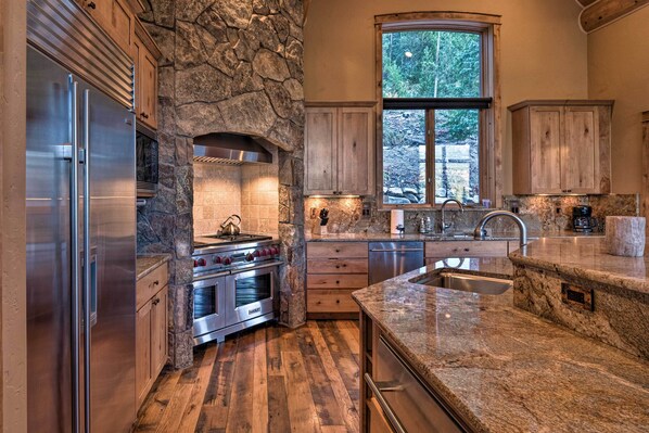 A kitchen with a stone wall, stainless steel appliances, a large window, and a granite countertop.