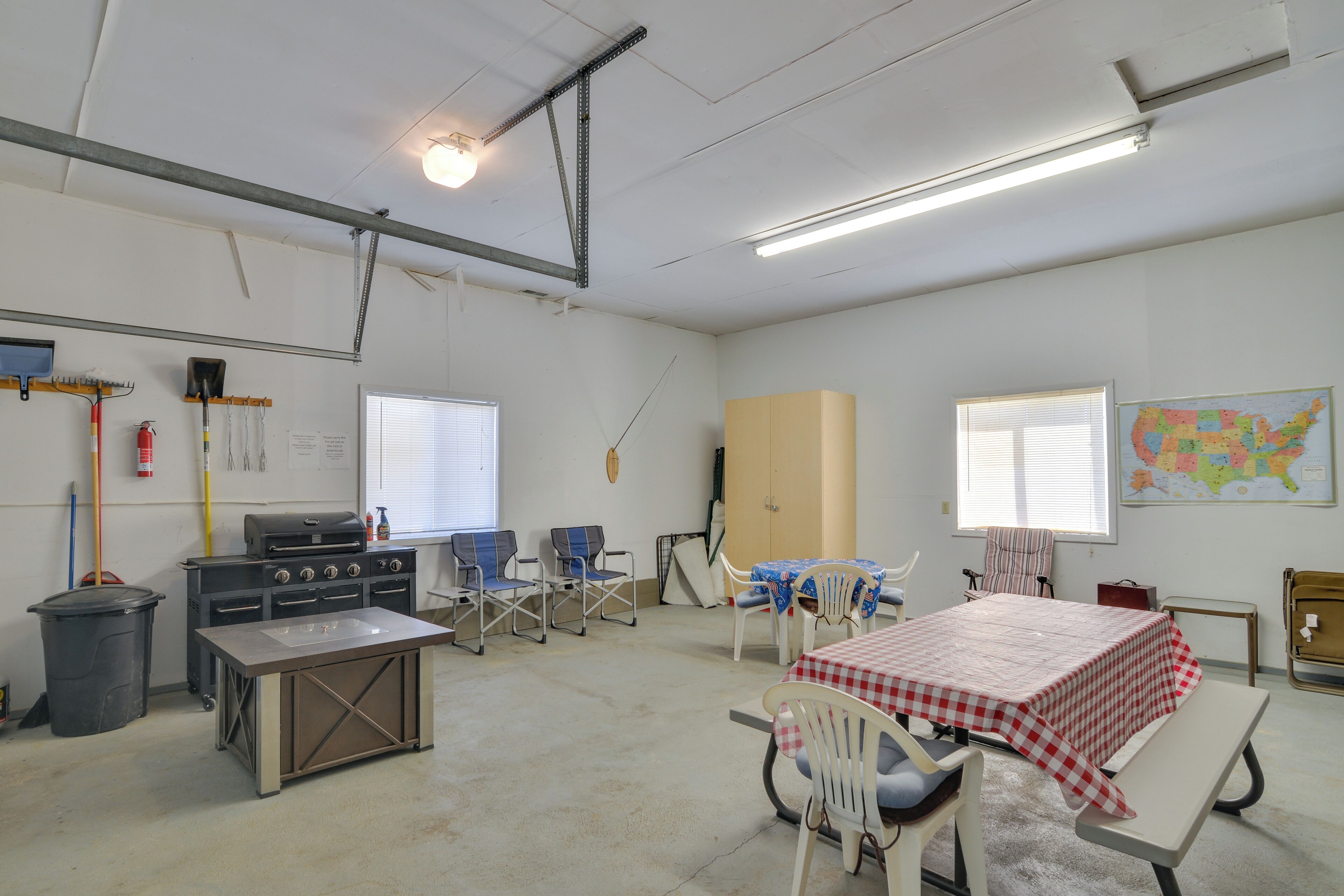 A spacious room with a kitchenette, a dining table with chairs, a map on the wall, and a window with blinds.