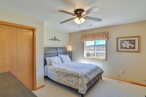 A bedroom with a bed, a ceiling fan, a window with a view, and a door.