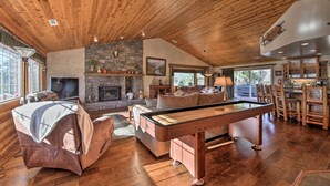 Una habitación acogedora con mesa de billar, asientos cómodos, chimenea de piedra y ventanas grandes.