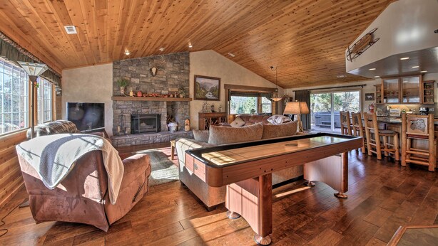Una habitación acogedora con mesa de billar, asientos cómodos, chimenea de piedra y ventanas grandes.