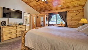 Una habitación tipo cabaña de madera con cama, televisor, cómoda de madera y ventilador de techo.