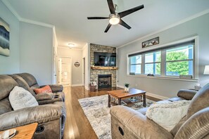 A living room with leather sofas, a fireplace, a ceiling fan, and a large window.
