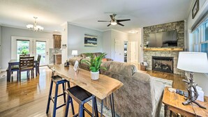 A spacious living area with a fireplace, a stone wall, and a large TV. - Striking Waynesville Home w/ Mtn Views & Deck (Waynesville)