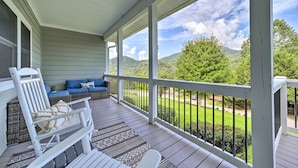 A covered porch with a white railing, a white rocking chair, a blue sofa, and a patterned rug. - Striking Waynesville Home w/ Mtn Views & Deck (Waynesville)