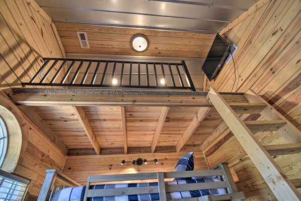 A wooden interior with a balcony, a ceiling fan, and a window. - Riverfront Cottage: Fire Pit & Kayaks (Deltaville)