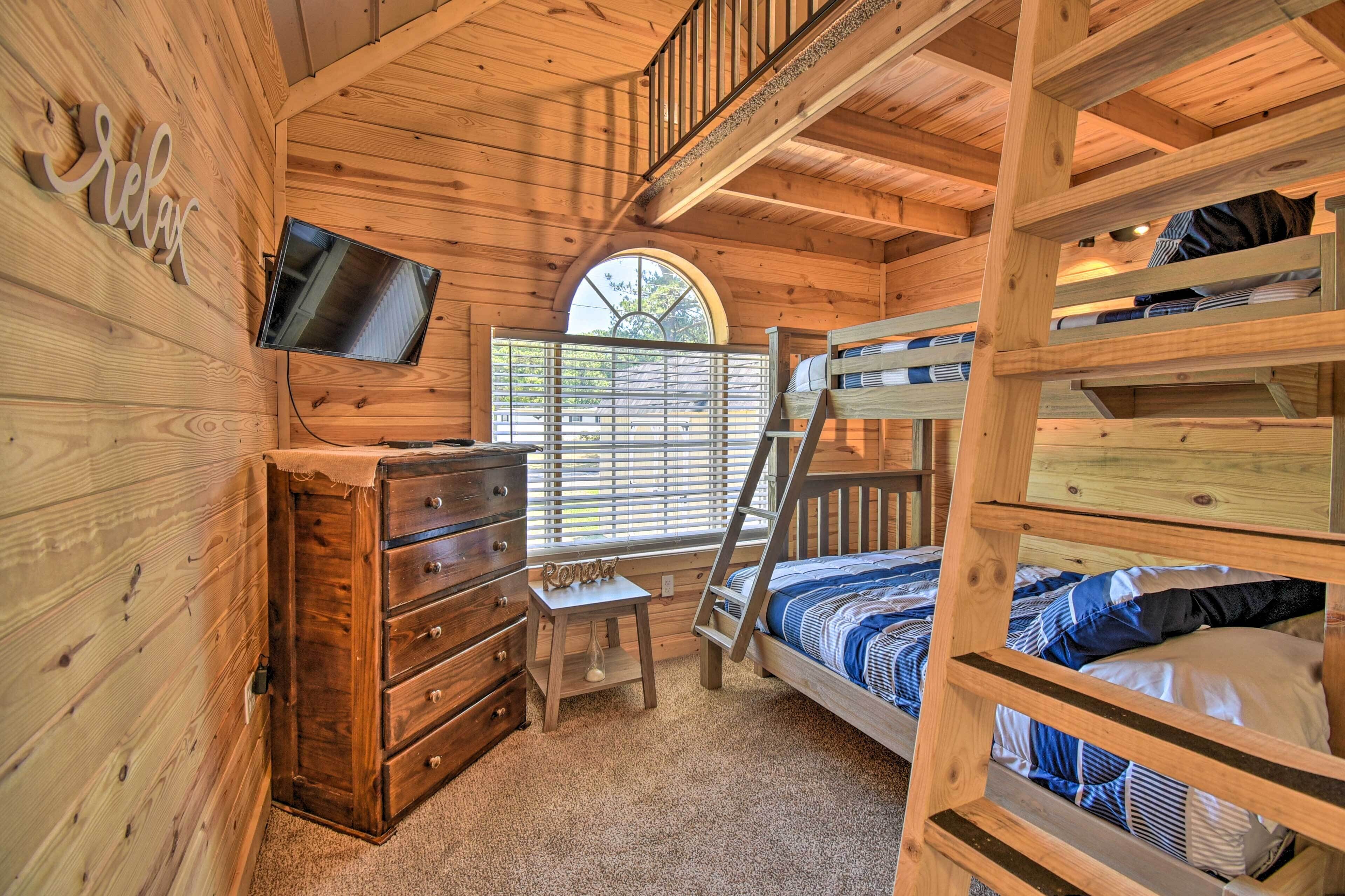Una habitación tipo cabaña de madera con una cama litera, un aparador, un televisor y una ventana con persianas.