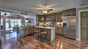 A spacious kitchen with wooden cabinets, a large island with bar stools, stainless steel appliances, and a ceiling fan. - Riverfront Cottage: Fire Pit & Kayaks (Deltaville)