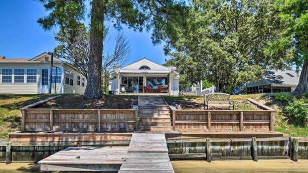 A wooden dock leading to a house with a covered porch and outdoor seating. - Riverfront Cottage: Fire Pit & Kayaks (Deltaville)